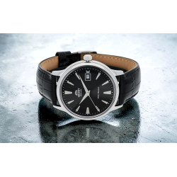 Czarny cyferblat, srebrne indeksy i datownik w automatycznym zegarku Orient Bambino TAC00004B0